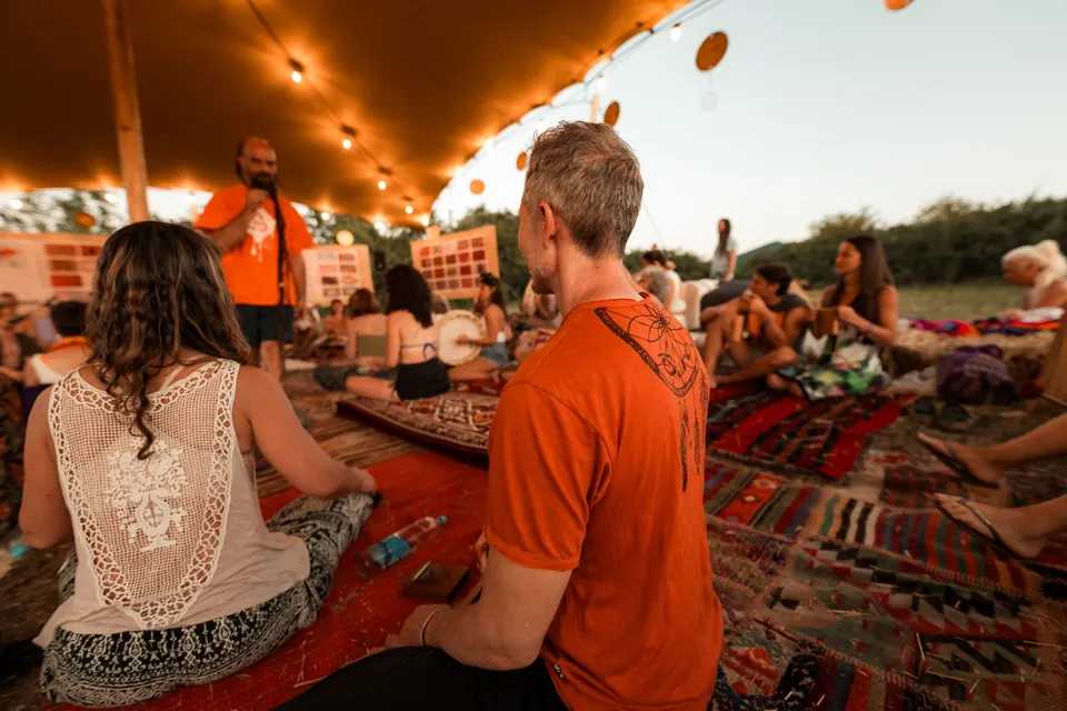 Musicians and listeners on rugs in the VRELO jam tent under string lights