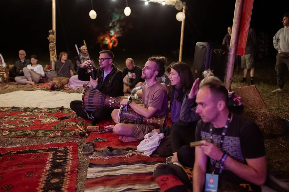 A night jam on rugs under string lights, djembe and voices in the VRELO tent