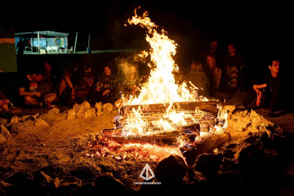 A campfire burning at night with people sitting around it