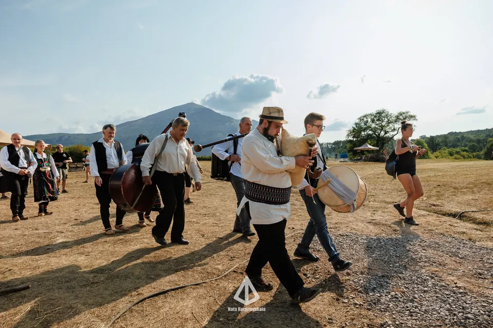 Folk musicians in costume walking across the meadow below Rtanj