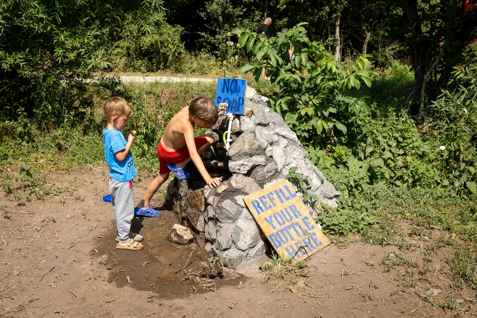 Children refilling water at the stone spring with a "refill your bottle" sign