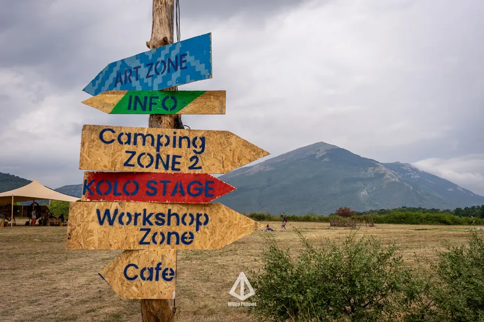Drveni putokaz ka Art Zone, Info, Camping Zone 2, KOLO Stage, Workshop Zone i Cafe, sa Rtnjem u pozadini.