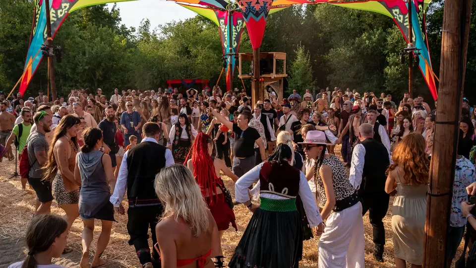 Festival visitors and dancers in traditional Serbian costumes joining hands in a kolo circle under the colourful canopy of the KOLO main stage at Pyramid Festival 2025.