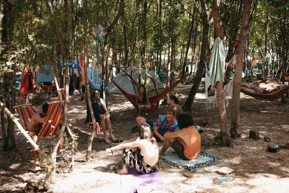 Posetioci festivala odmaraju u hladu drveća, među visećim mrežama
