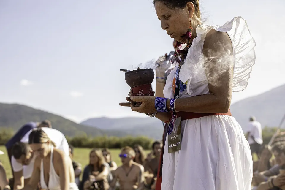 A woman in white carries a smoking bowl through the ceremony