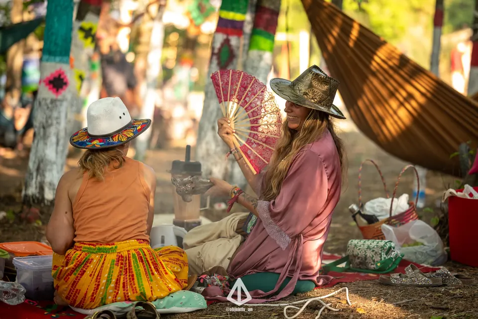 Two women with fans resting in the shade of the forest
