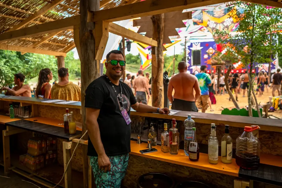 Posetioci festivala za drvenim šankom pod krovom od trske, sa festivalskim prostorom iza njih.