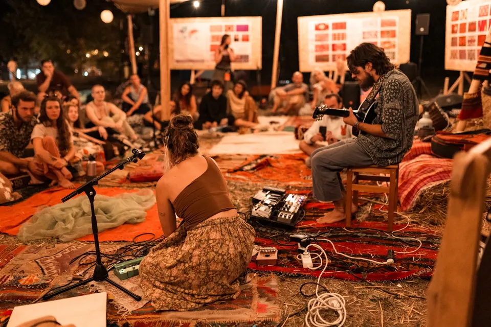 Musicians and listeners sitting on rugs at a VRELO jam session under the tent