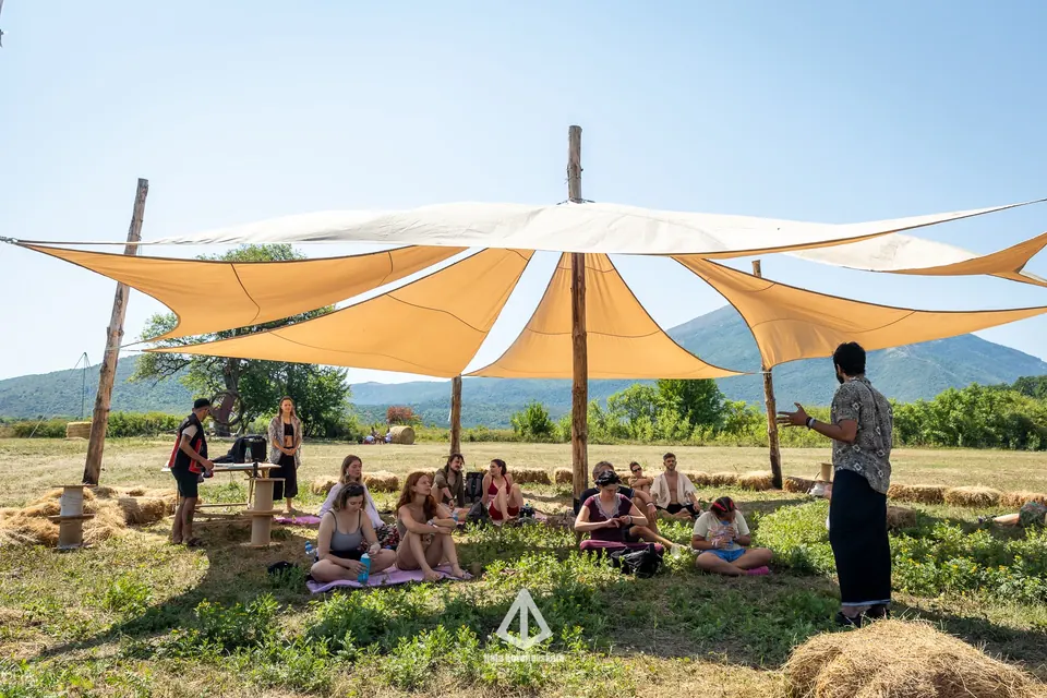 A workshop gathering under white shade sails on the grass